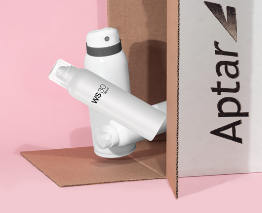 A white spray bottle labeled WS30 by Aptar, featuring Aptar's contemporary aerosol actuator designed for e-commerce-capable packaging, rests beside another white bottle and an Aptar-branded cardboard box.