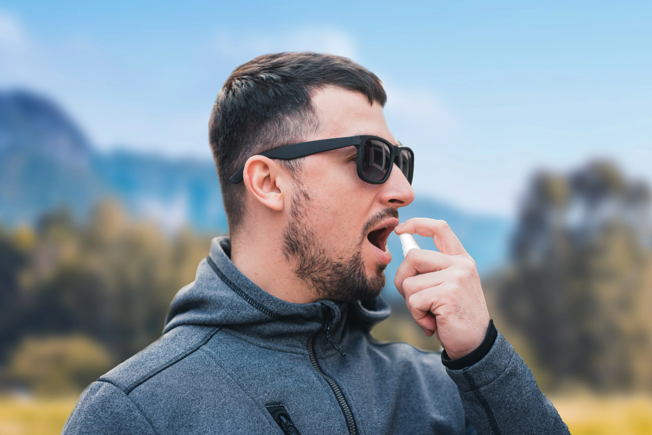 Adult man wearing sunglasses uses Aptar Pharma oral liquid dispenser in outdoor setting for VMS product.
