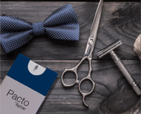 A blue polka dot bow tie, silver scissors, a safety razor, a shaving brush, and Pacto Lotion pocket-size beauty packaging, cardholder are arranged on a dark wooden surface.