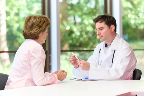Male physician in white lab coat explains Aptar nasal vaccine device to female patient in doctor's office setting.