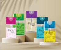 Five Purette Fine Mist bottles with  flat mini spray packaging are labeled Pacto by Aptar in pink, green, purple, blue, and yellow sit on round beige pedestals against a neutral background.