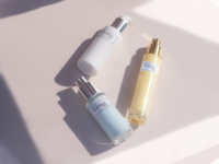 Three chic and premium cosmetic pump bottles labeled EVOLUX rest on a pale pink surface, including a white bottle and two translucent bottles filled with blue and yellow liquids.
