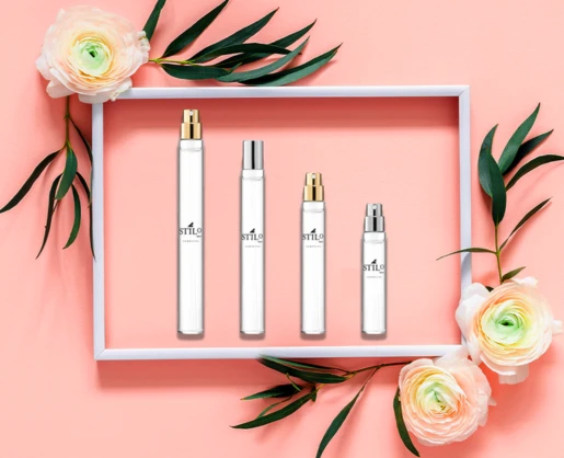 Four white perfume bottles labeled Stilo, featuring a Refillable Fragrance Mini Packaging, are arranged in a white rectangular frame decorated with green leaves and cream-colored flowers, all set on a peach background.