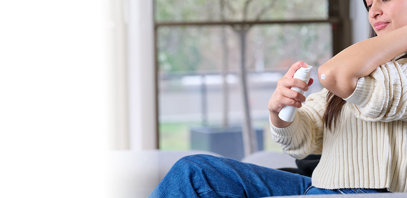 Close up of woman's face dispensing dermal product on elbow from small white Aptar Pharma Airless+ drug delivery system