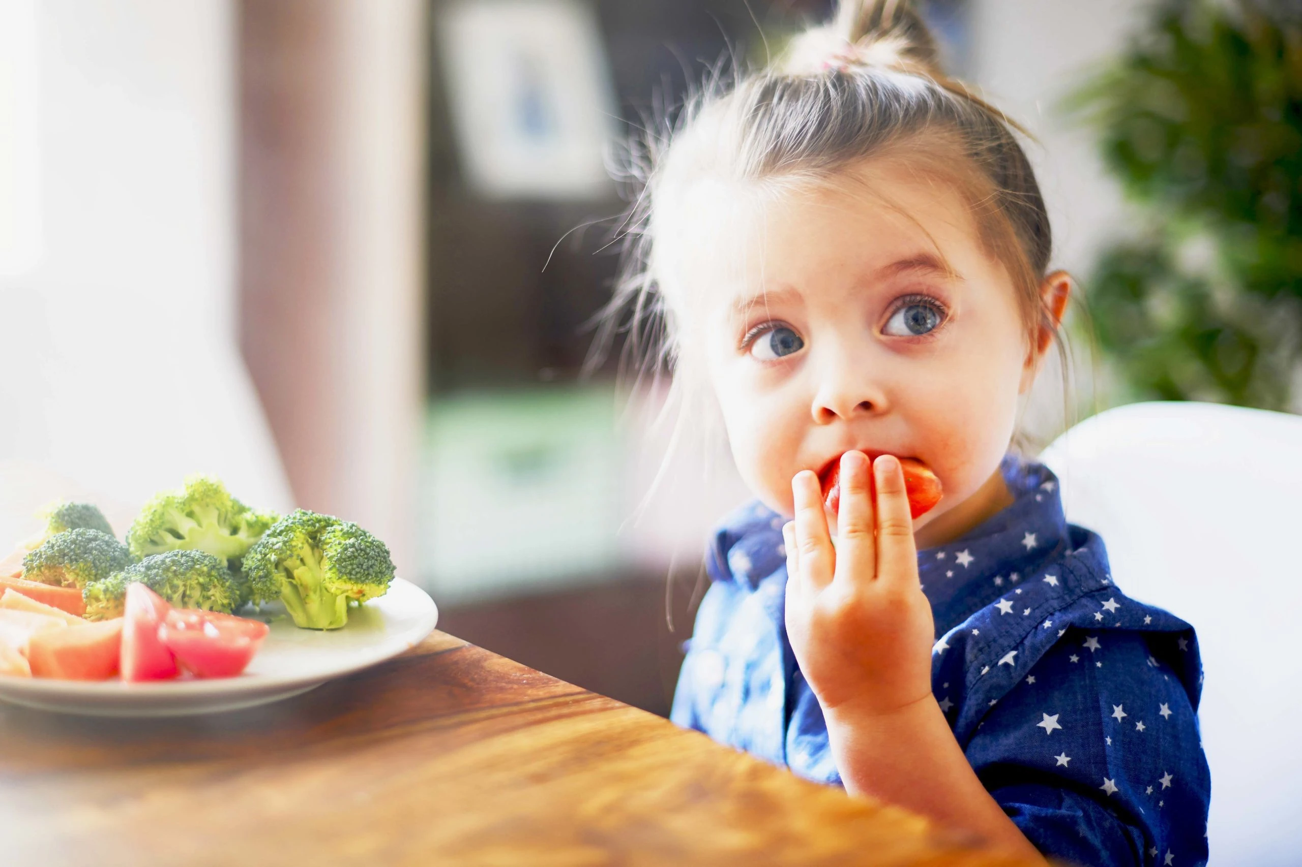 Young girl eating vegetables at kitchen table