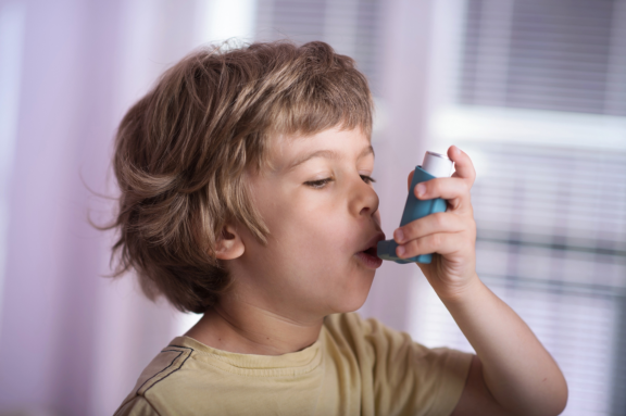 Young boy with light brown hair uses an inhaler containing an Aptar DF30 metering valve to deliver asthma medication.