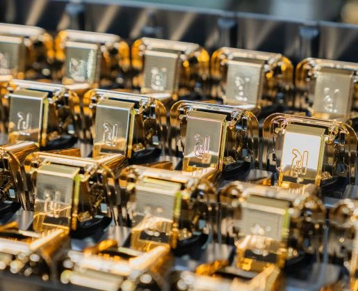 Rows of shiny gold metal components, reminiscent of custom primary beauty packaging, are neatly arranged in a tray, reflecting light and creating a futuristic, high-tech appearance.