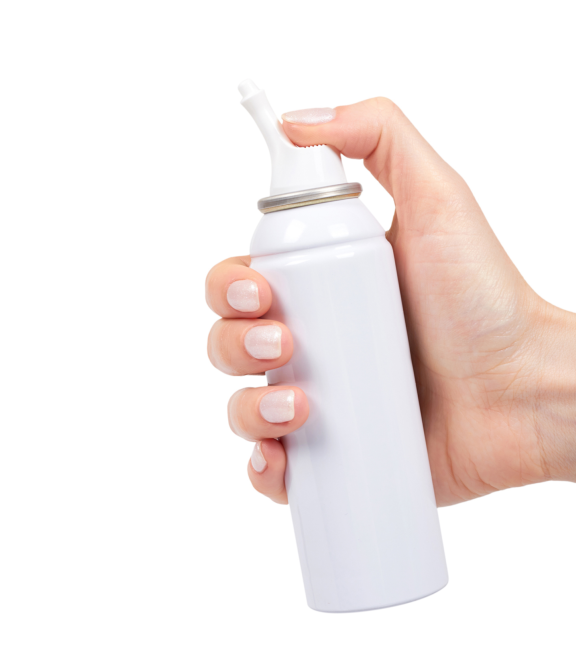 A hand holding and actuating a white bag-on-valve spray can. The user’s thumb presses down on the nozzle, demonstrating the ergonomic design of the actuator for controlled dispensing.