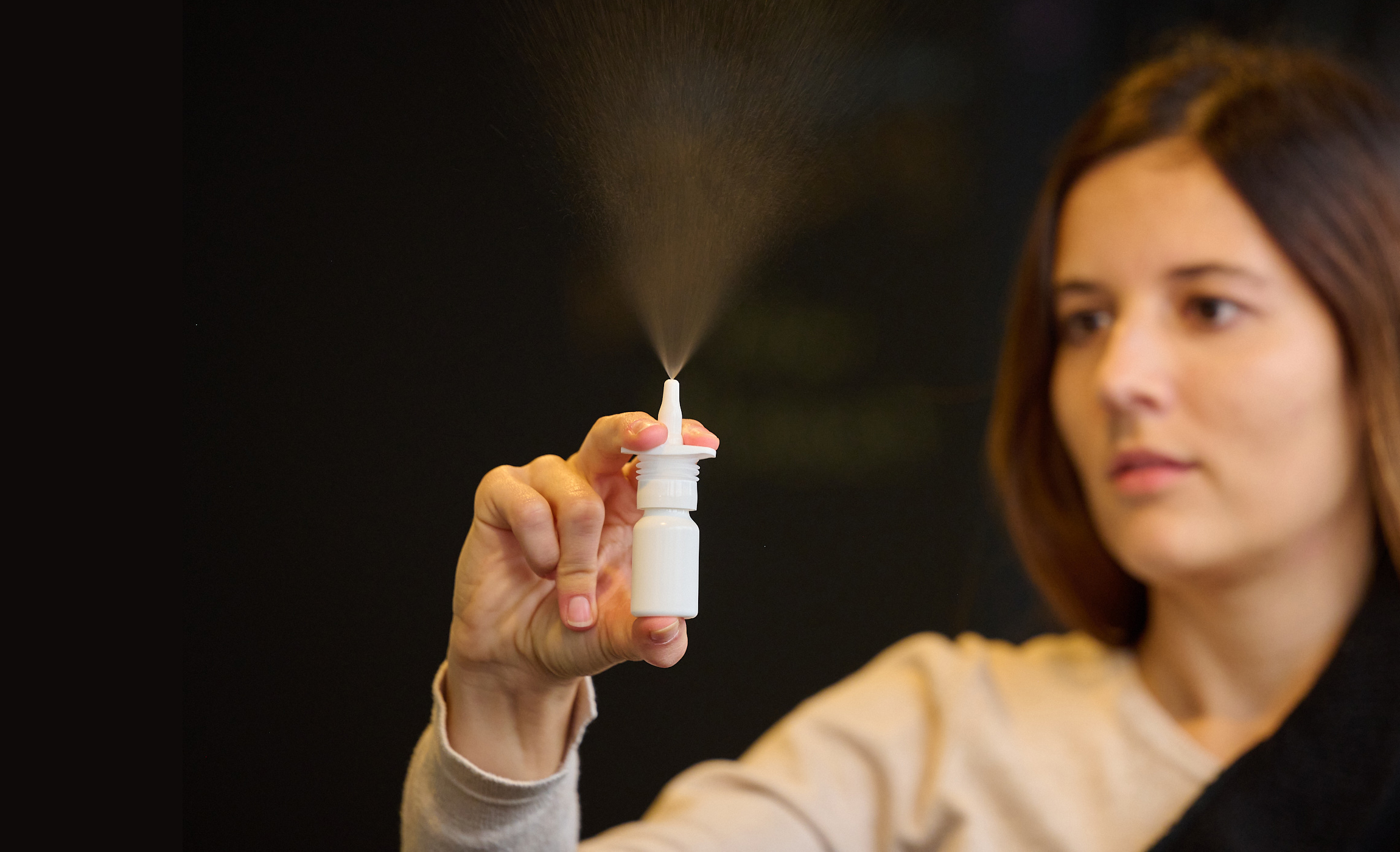 Standing woman with brown hair dispenses nasal spray in the air showing spray plume from APF futurity.
