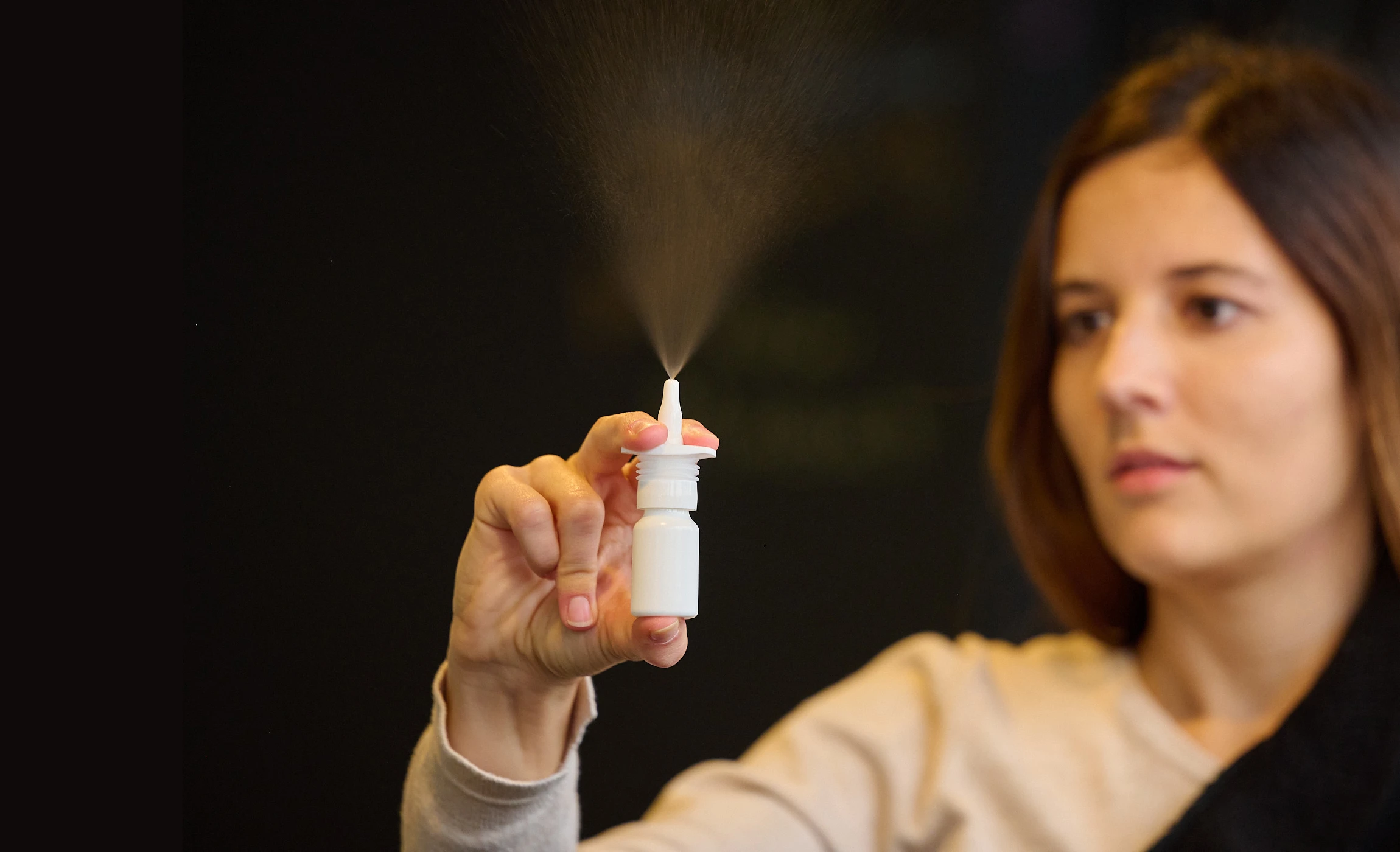 Standing woman with brown hair dispenses nasal spray in the air showing spray plume from APF futurity.