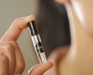 An Easy Spray fragrance sampling vial is held between two fingers in a close-up view, demonstrating a compact spray format for fragrance discovery and product trial.