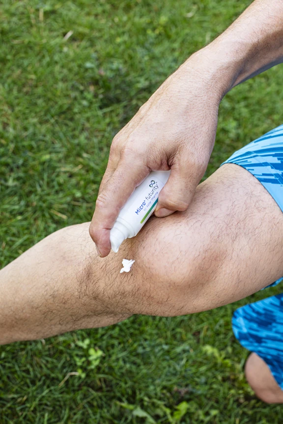 White recyclable Aptar Pharma Micro+ Futurity dispenser used by man to dispense cream formulation onto leg in grass field.