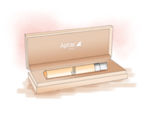 A rectangular beige box labeled Aptar beauty is open to display a Stilo, a refillable fragrance mini packaging by Aptar with a silver cap, resting inside a custom-fitted slot.