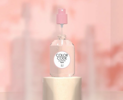 A clear glass bottle with a refillable plastic fragrance pump labeled Color Code Screw sits on a cylindrical pedestal against a soft pink, blurred background.