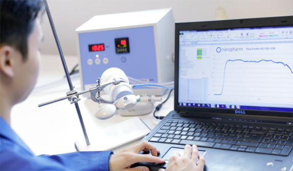 Gloved hands operating a computer running specialized analytical testing on Aptar DPI solution based product attached to stand.