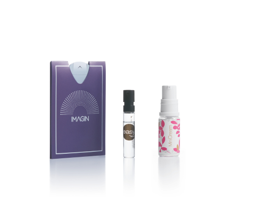 A purple flat rectangular sample  labeled IMAGIN stands next to mini packaging labeled Minicream a small glass vial with a black cap and a small white spray bottle with a pink floral design all set against a white background.
