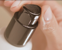 A close-up of a hand pressing a black twist-to-lock spray pump on a white bottle with a  named PZ Twist, possibly for skincare or liquid soap, as natural light gently illuminates the fingers and the dispenser.