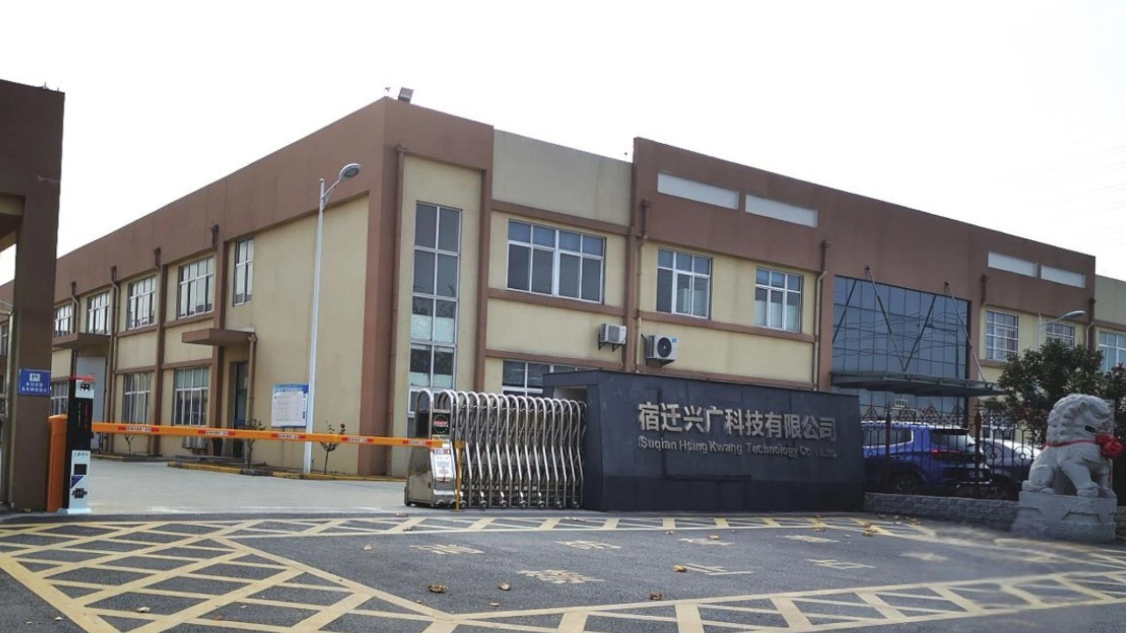 A picture of BTY's Hsing Kwang Suqian aluminum manufacturing factility. A beige and brown industrial building with large windows and a retractable gate at the entrance. There is a sign with Chinese characters and the English text Shenzhen Huaying Huaxing Technology Co., Ltd.