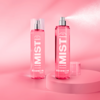 Two pink bottles labeled Fragrance MIST from the Essencia Collection, featuring an elegant fragrance pump, are displayed on a pink surface. One bottle has a cap on, while the other sprays a fine mist against shades of pink in the background.