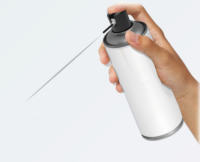 A hand holds and sprays an aerosol can with a blank white label, featuring an Aerosol Actuator with Built In Tube named Akur, releasing a fine mist through a narrow nozzle against a plain light background.