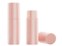 Two pink cylindrical face stick containers are shown; one is fully closed, and another is open with the cap removed and placed beside it, revealing the product inside. These smooth matte containers highlight a custom cosmetic packaging manufacturer's design.