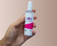 A person holding a clear bottle fitted with a Lotion cosmetic pump. The pump is uncapped, revealing the actuator, and the label 'Click by Aptar' is printed on the front of the bottle.