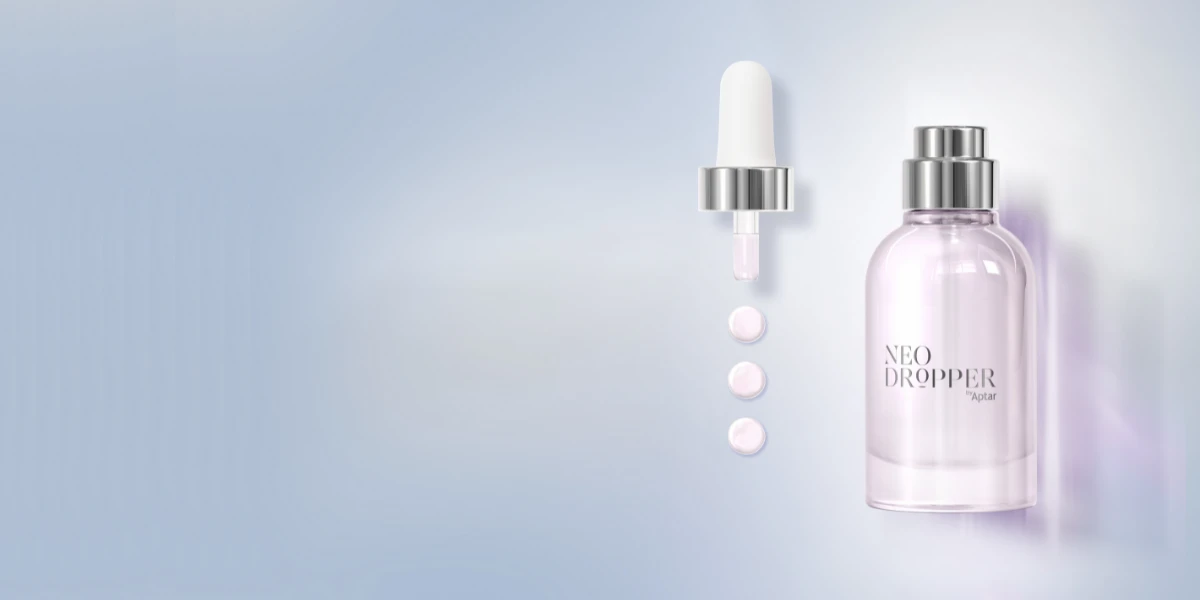 A clear glass bottle with dropper packaging labeled NEO DROPPER by Aptar stands next to a dropper releasing three pink drops, set against a light, soft gradient background.