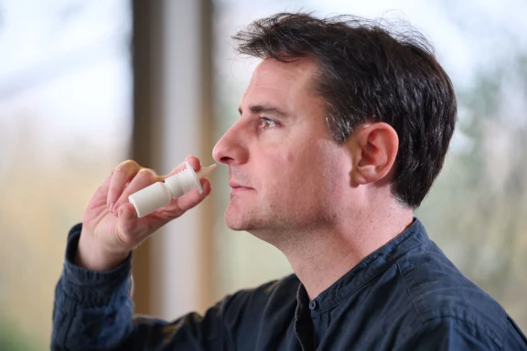 Man with short brown hair holding APF futurity recyclable nasal spray to nose to administer dose.