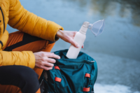 Person kneeling outdoors removing a white PureHale fine mist dispenser with clear mask from a green backpack.