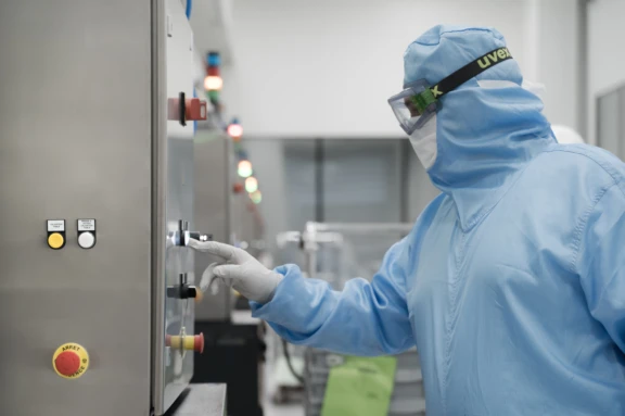 Operator in cleanroom gown adjusting industrial control panel in injectable manufacturing environment