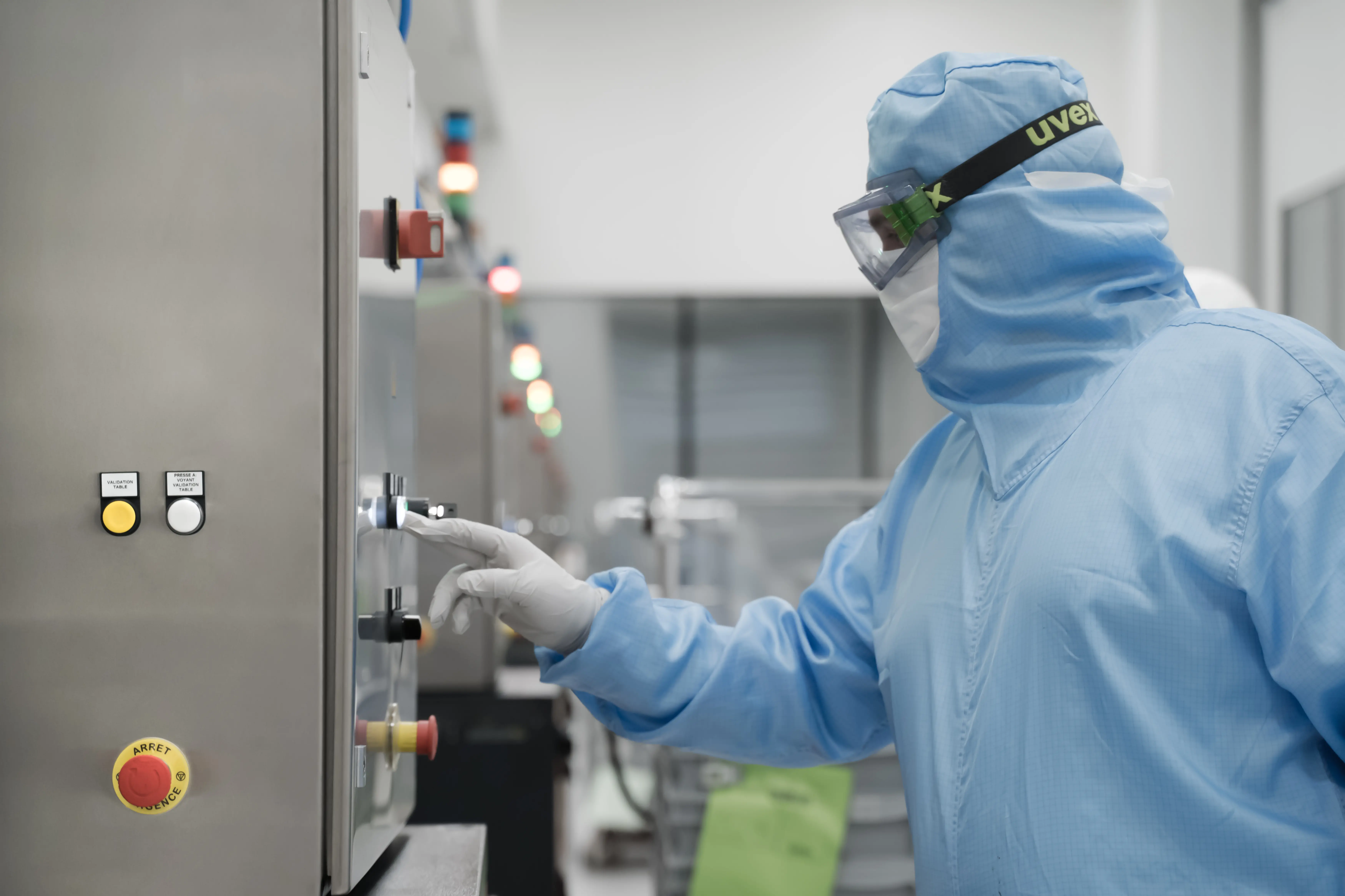 Operator in cleanroom gown adjusting industrial control panel in injectable manufacturing environment