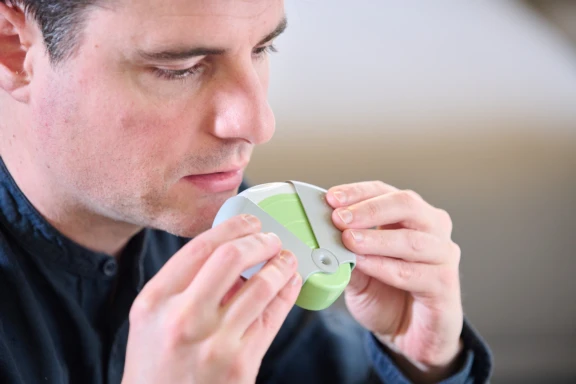 Close up of man in dark shirt holding green Aptar Pharma ProHaler multidose dry powder inhaler to mouth for administration.