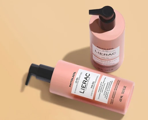 Two pink pump bottles of Lierac Phytolastil Gel rest on a beige surface, one upright and the other lying down, both featuring EuroFlow Standard, a high performance dispensing pump and clearly displaying the product label.