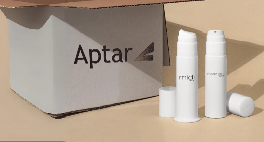 A cardboard box labeled Aptar sits next to two white plastic bottles labeled Midi and Macro Slim, designed with airless packaging for high-viscosity formulas, with their caps placed nearby on a beige background. The image indicates the products are designed for omnichannel shipping needs.
