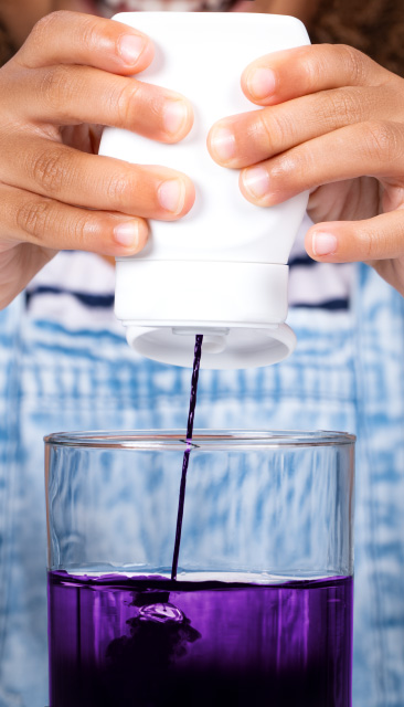 Squeezing purple concentrate into a glass of water using Aptar's dispensing closure