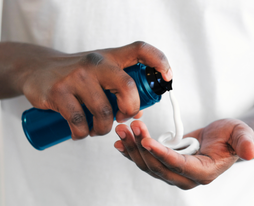 A person dispenses white lotion or cream from a navy blue bottle with an Aerosol Actuator for Foam and Gel named Optimum onto the palm of their hand, with a white shirt visible in the background.