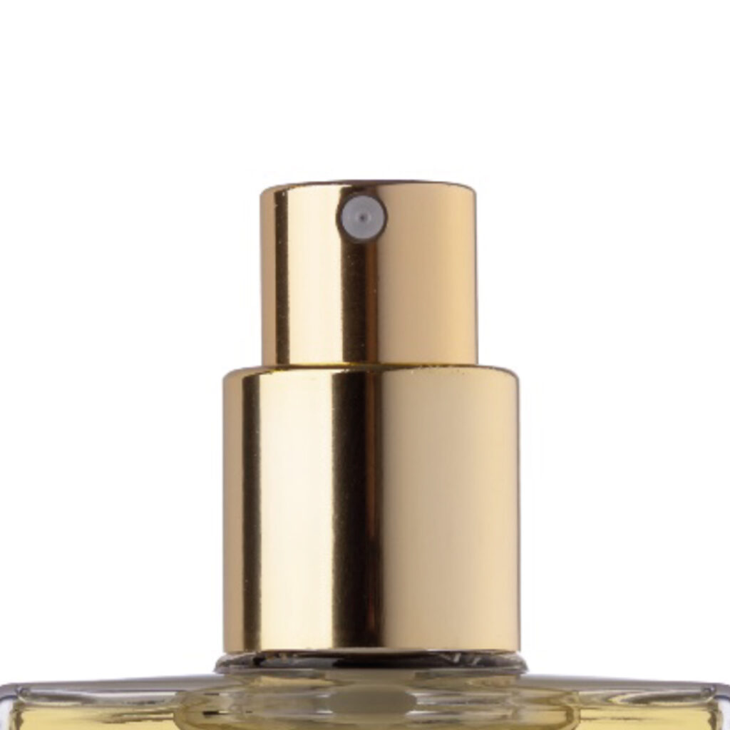 Close-up of a gold-colored spray pump for dry oils named Oil Mist on top of a glass perfume bottle, set against a white background.
