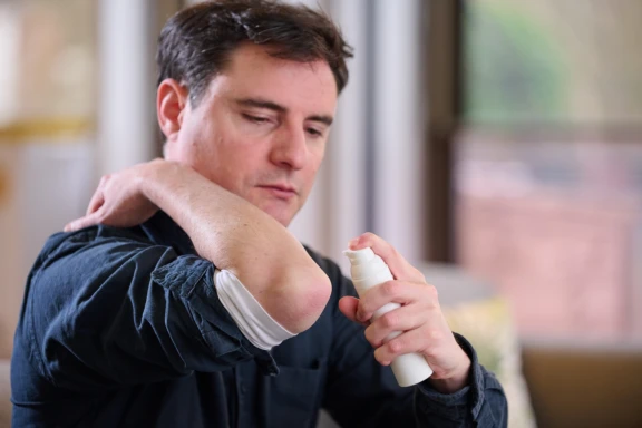 Man with dark hair and blue sweater dispenses dermal drug product from Aptar Airless+ pump on elbow in office