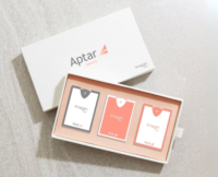 A rectangular white Aptar Beauty box is opened to reveal three ultra-flat fragrance sampling cards labeled 'Imagin', neatly arranged inside. The design showcases the suitability of the sampling solution for premium packaging.