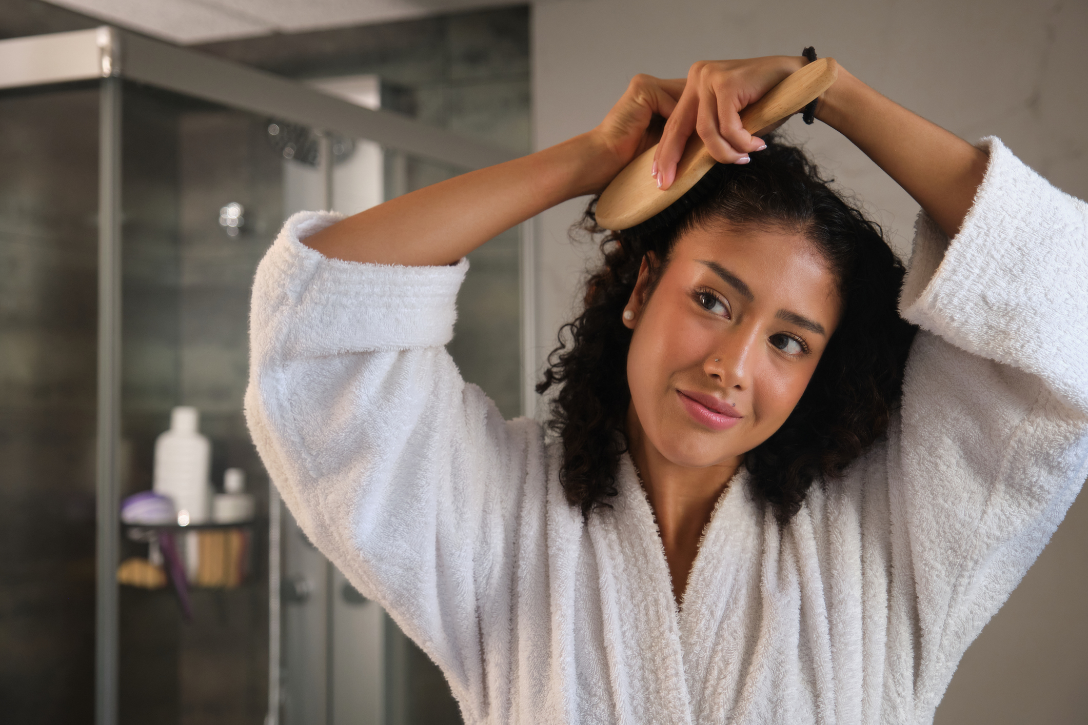 Young woman brushing curly hair in bathroom after shower