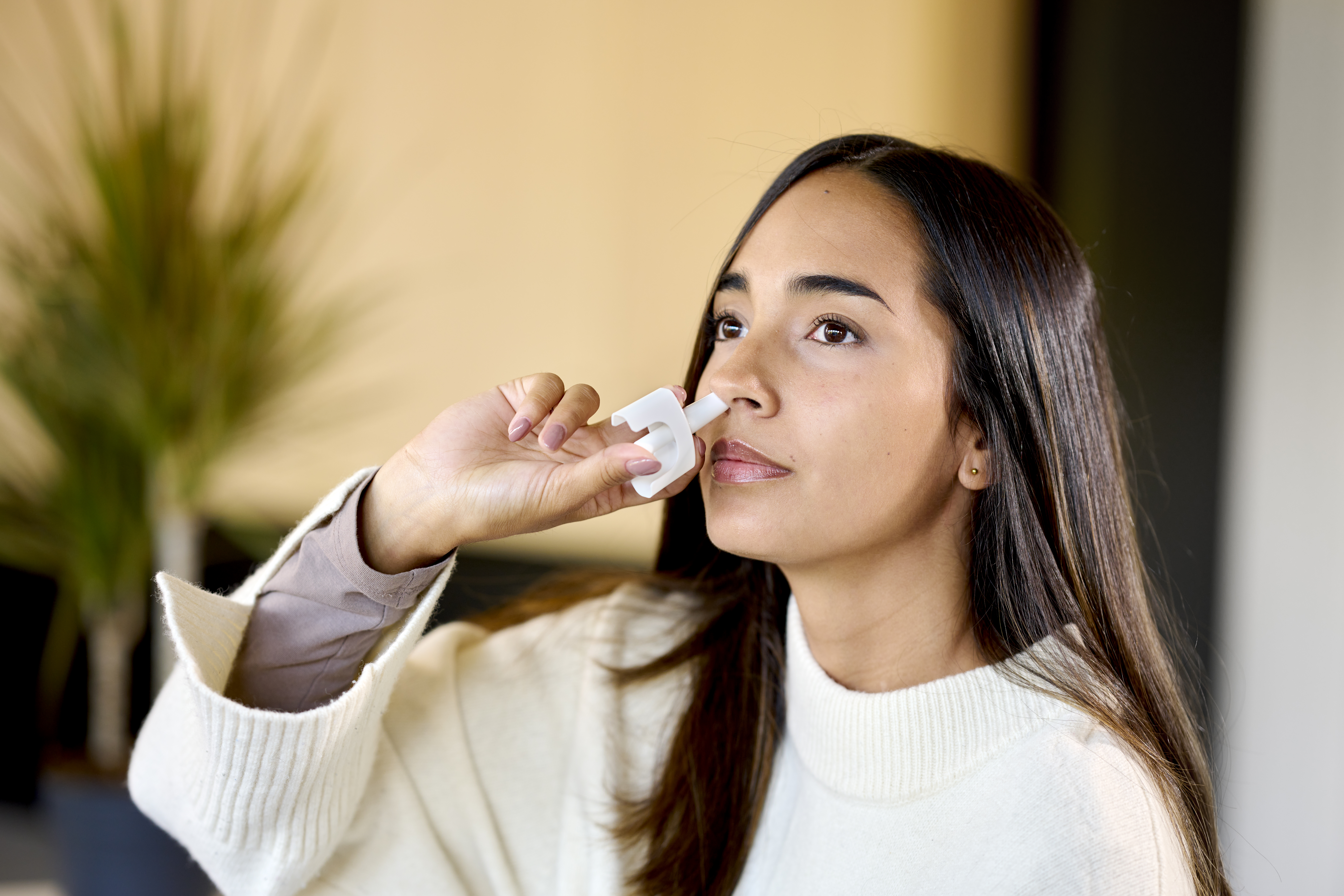 Woman in white jacket administers a single precise dose from an Aptar Unidose liquid nasal spray device zoom view