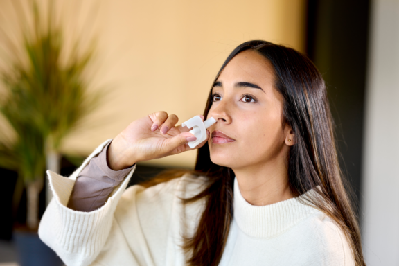 Woman in white jacket administers a single precise dose from an Aptar Unidose liquid nasal spray device zoom view