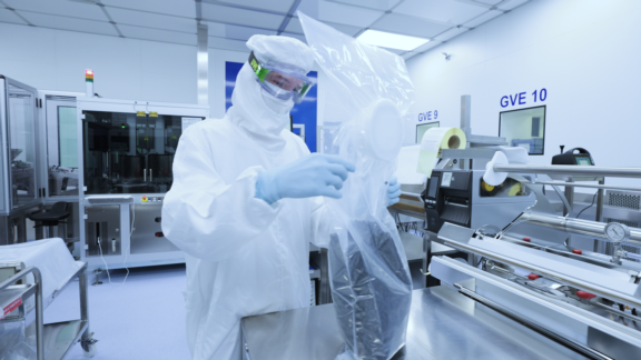 Fully gowned Aptar Pharma laboratory operator handles a RTP PE bag for RTU gamma sterilized injection components.