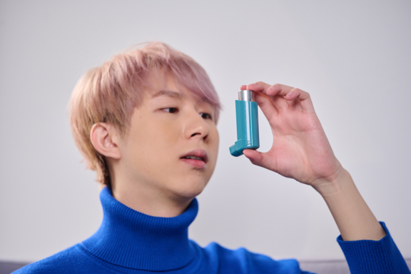 Patient holding blue and white Aptar inhalation solution with DF30 to mouth wearing blue sweater with light hair.