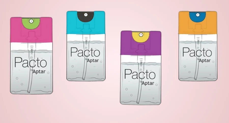 Four Purette Lotion  spray bottles with flat mini packaging are labeled 'Pacto by Aptar' are arranged side by side, each featuring a different colored top: pink, blue, orange, and purple , set against a light pink background.