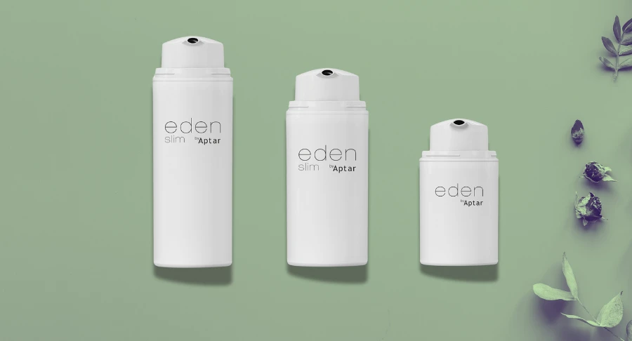Three white airless bottles labeled Eden Slim by Aptar, featuring airless packaging for skincare, are arranged from tall to short on a light green background, with green leaves and herbs placed on the right side.