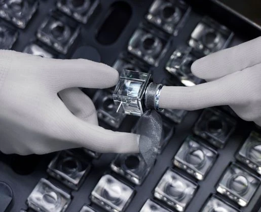 Gloved hands carefully inspect a clear, square fragrance over cap in a tray filled with the same clear, square fragrance over cap suggesting meticulous quality control in a setting reminiscent of custom primary beauty packaging  manufacturing processes.