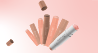 Several Duo Flash mono-material face sticks in neutral and pink tones stand upright and tilted on a light pink gradient background, with two caps floating nearby.