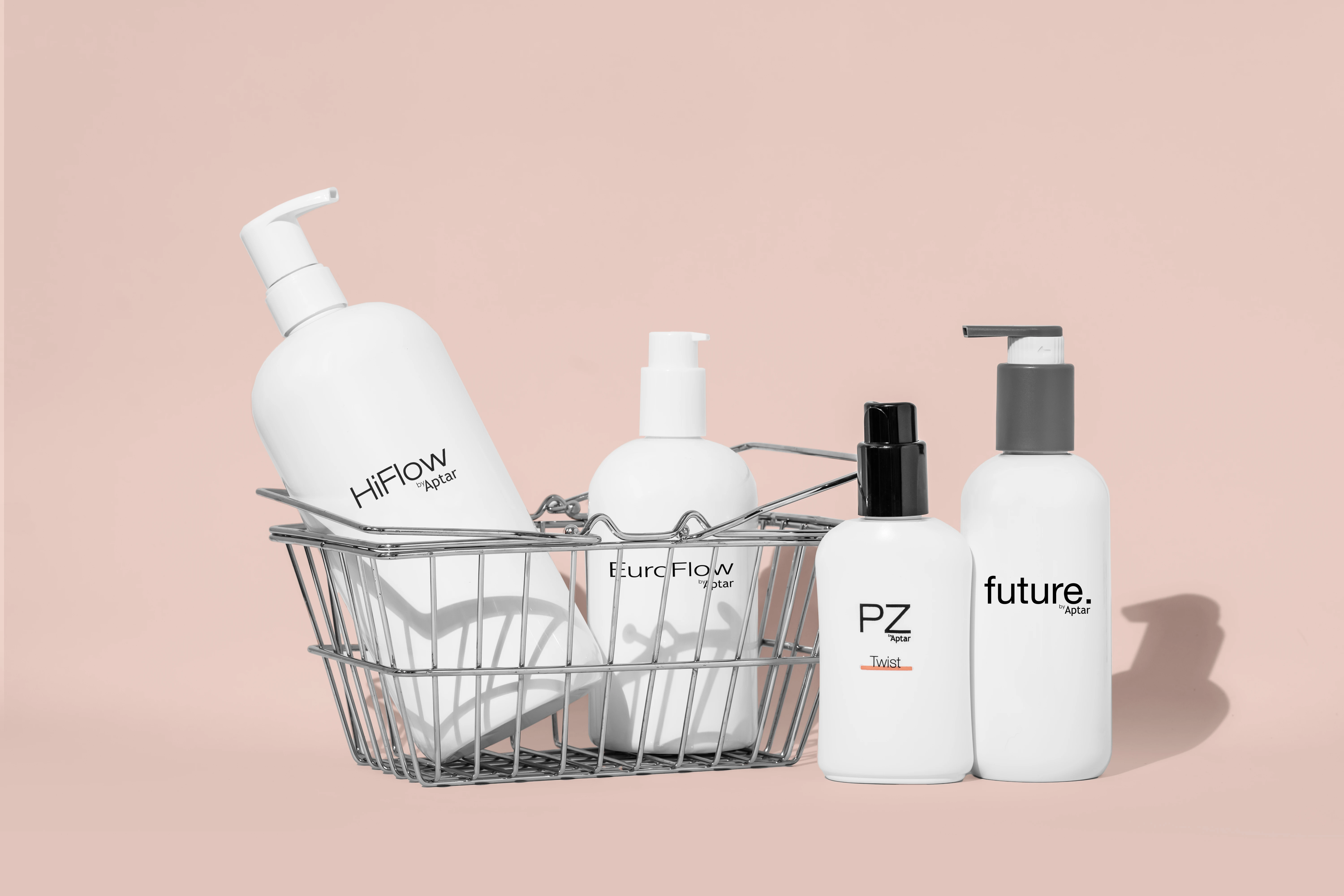 Four white high performance dispensing pump bottles labeled HiFlow, EuroFlow, PZ, and Future are arranged in and beside a small wire basket, set against a pale pink background.