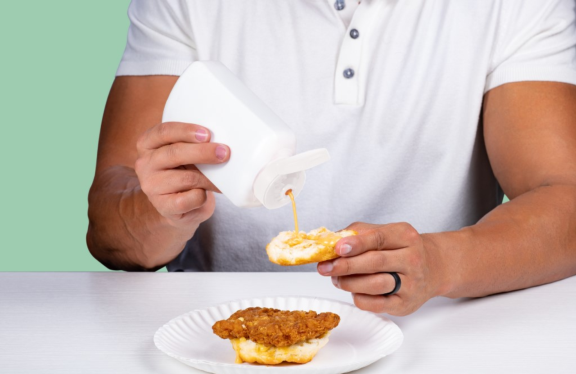 Man squeezing chick fil a sauce onto a chicken sandwich